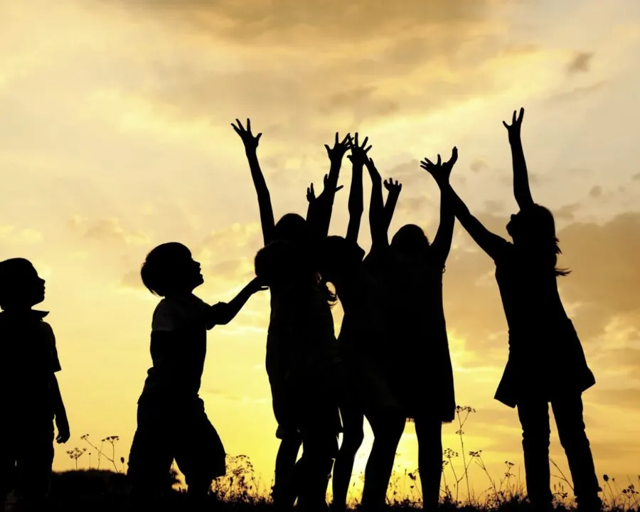 Silhouettes d'enfants les bras levés au coucher du soleil — REBSL, réseau petite enfance
